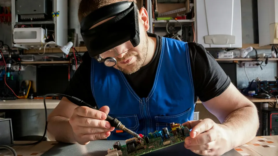 Elektroniker lötet mit Lupenbrille an einer Platine